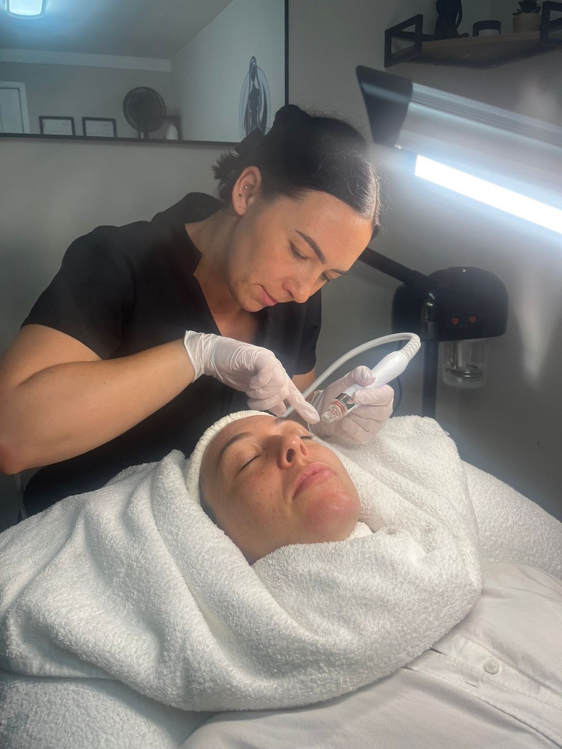 Leya Lopez working across a client's forehead with the HydraFacial handpiece, the client wrapped in a warm towel